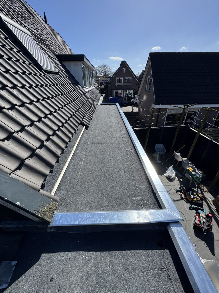 Nieuw bitumen plat dak met daktrim naast pannendak van woning in Apeldoorn