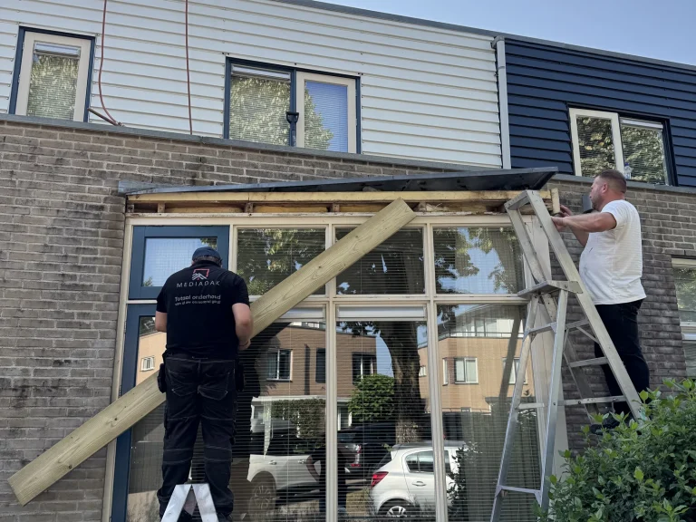 Twee dakdekkers monteren het nieuwe boeideel boven een grote raampartij in Beekbergen
