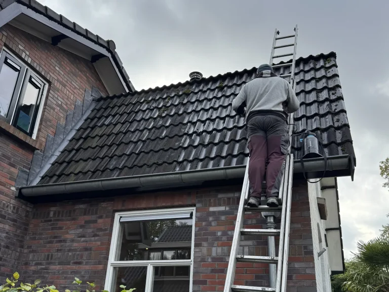 Dakdekker op ladder bij een vervuild donker pannendak in Apeldoorn voor het reinigen